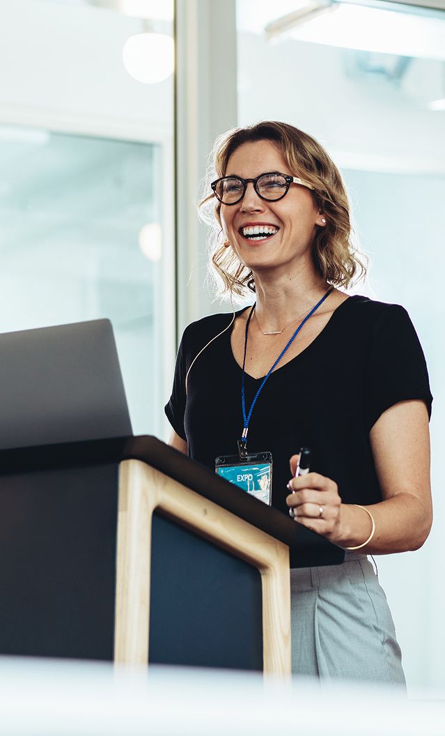 Eine Frau mit Brille steht an einem Rednerpult und spricht zu einem Publikum.